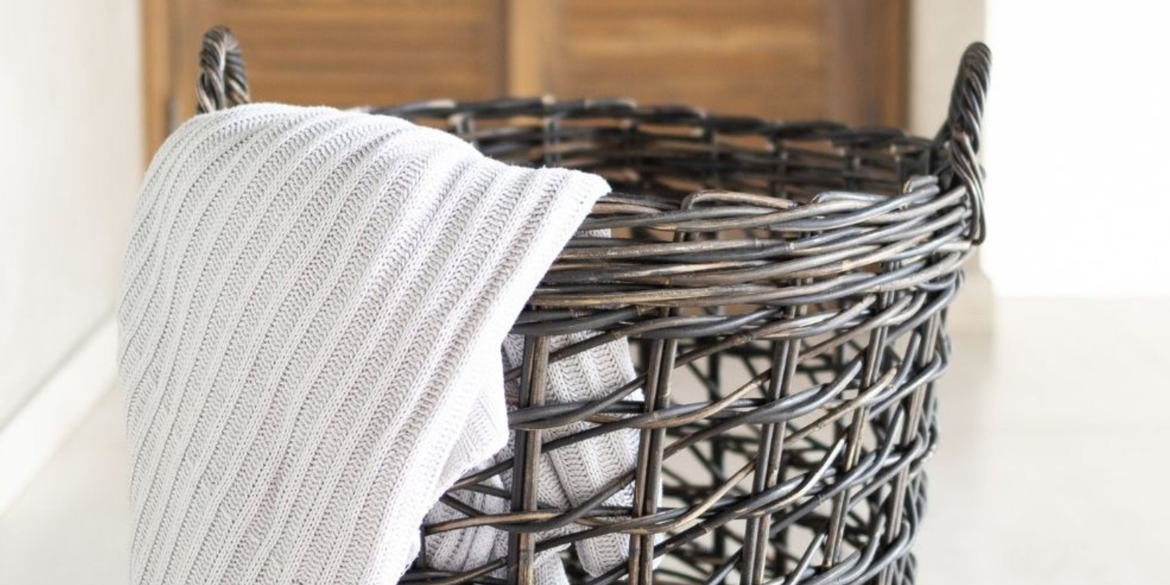 Black open weave rattan basket with overhanging white throw.